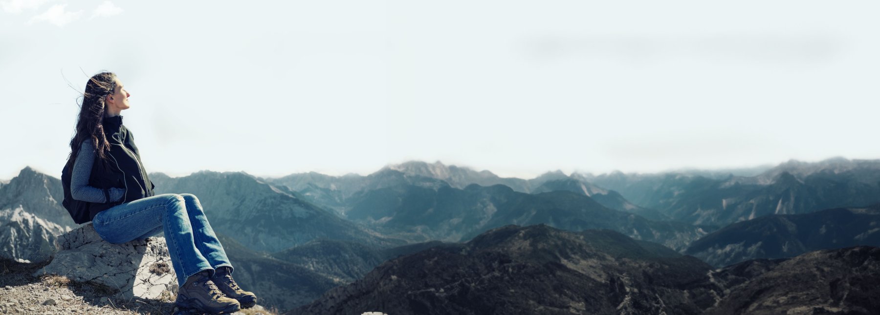 Frau auf einem Berggipfel hält ihr Gesicht cor einem Bergpanorama mit geschlossenen Augen in die Sonne.